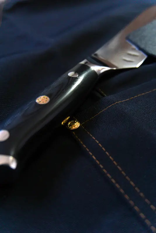 Santokumesser mit schwarzem G10-Griff liegt auf blauer Kochschürze – edles Design trifft auf Präzision.